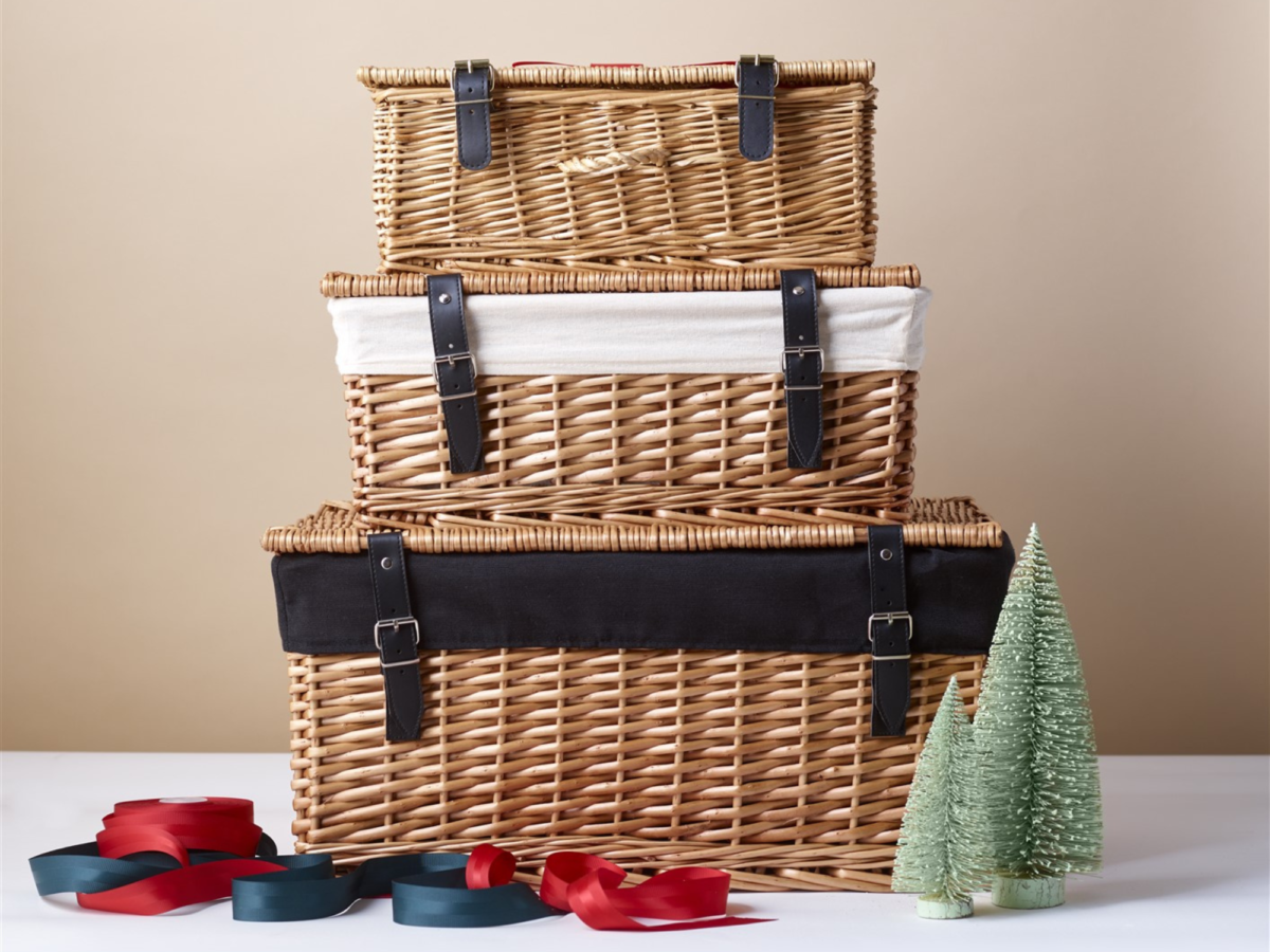 Three wicker hamper baskets each stacked one on top of each other with Christmas ornaments around it.
