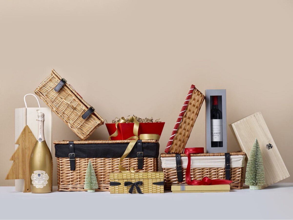 Selection of wicker hampers and trays, cardboard gift boxes, and wooden gifting boxes on a plain background with Christmas decorations