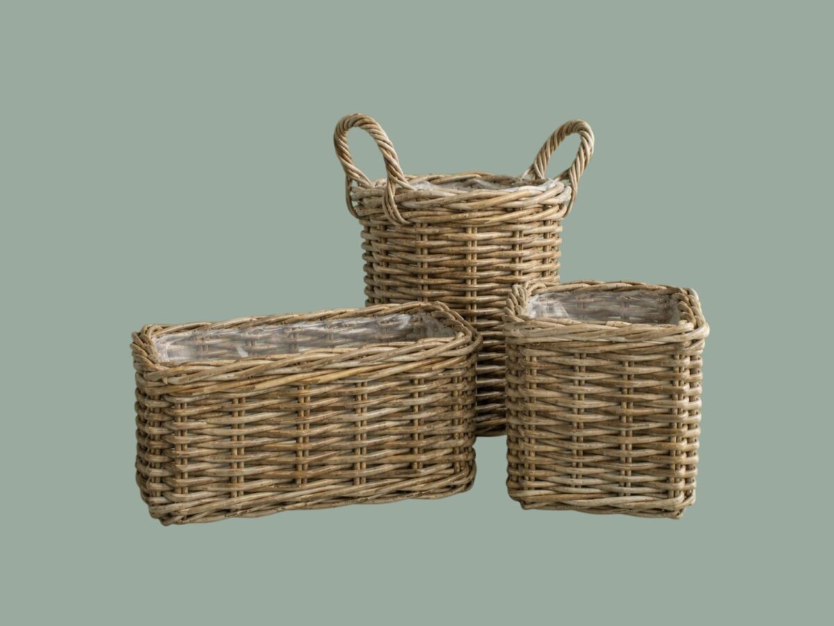 Three woven baskets of varying sizes and shapes against a muted green background. The largest basket in the back has two handles, the basket on the left is rectangular and the one on the right is square.