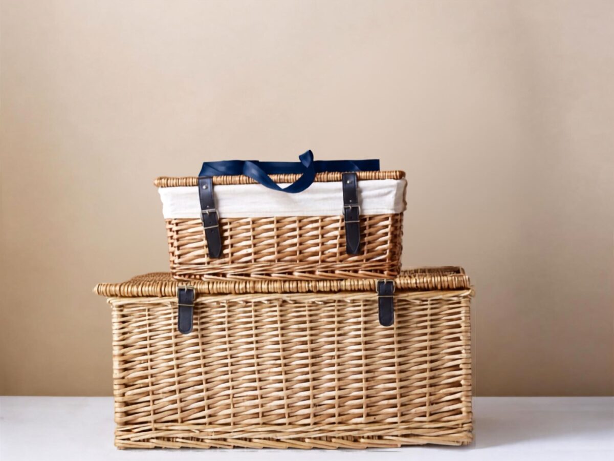 Two wicker hamper baskets stacked one on top of the other with the smaller top hamper featuring a cotton liner and blue ribbon on top