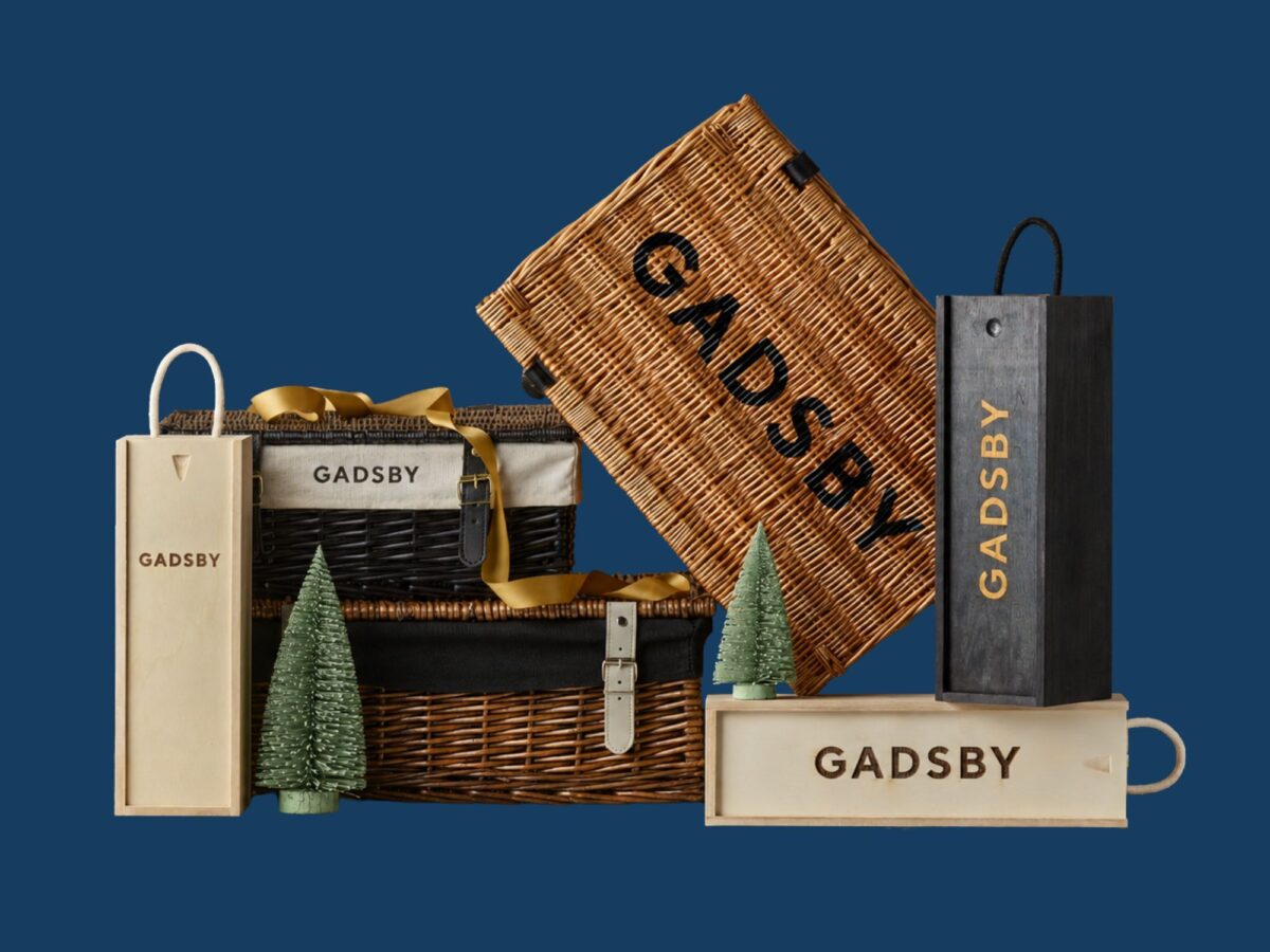 Selection of wicker hamper baskets and wooden bottle boxes that have been branded with Gadsby wording and small ornamental Christmas trees