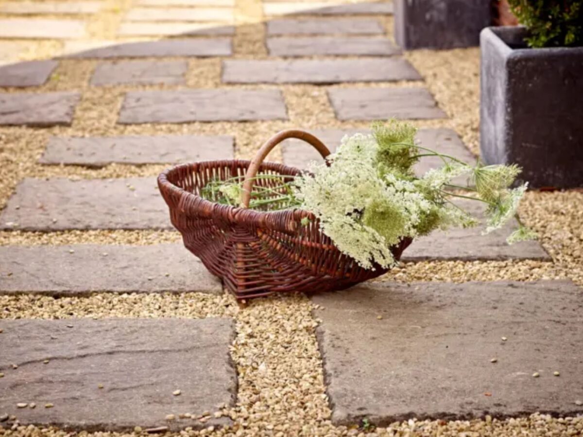 Wicker garden trug on a gravel pathway filled with greenery