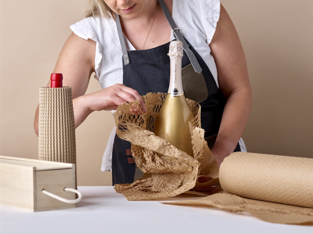A woman is shown wrapping protective transit paper around a bottle reading for sending to a customer