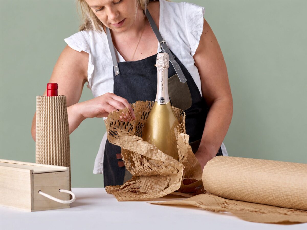 A woman wrapping a wine bottle with corrugated protective packaging.