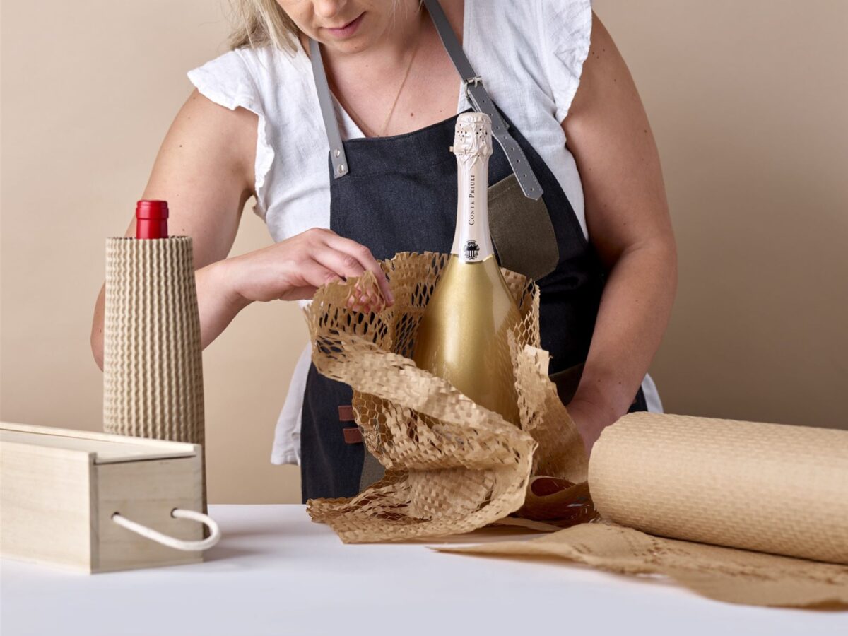 A woman using honeycomb paper to wrap a bottle of wine before putting into transit packaging